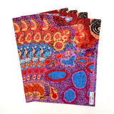 A stack of four folded sheets of wrapping paper featuring a vibrant Aboriginal dot art pattern with red, orange, blue, purple, and black dots on a white background.