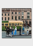 An old building with a green and yellow tram and people waiting on the street.