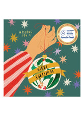 Christmas card with a hand holding a decorated ornament and colorful stars on a green background.