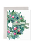 A wreath in greens and pink with a banner saying Comfort and Joy.