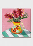 Orange vase with flowers on it and grevillea in it on a table with a green and white striped tablecloth.