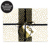 A gift wrapped with white paper with gold spots and black and gold ribbon.