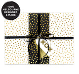 A gift wrapped with white paper with gold spots and black and gold ribbon.