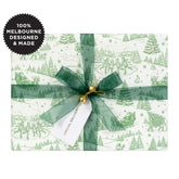 A gift wrapped in a green Christmas scene on white with a green ribbon.