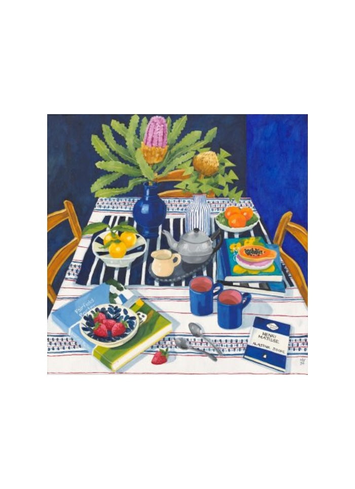 A blue vase with flowers on a table with tea things and books.