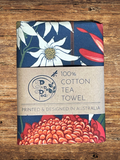 Floral patterned tea towel with branding on a wooden surface