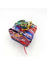 A small gift box wrapped in a vibrant, multicolored patterned paper with a rainbow-colored paper ribbon bow on top, set against a plain white background.