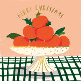 Illustration of oranges on a plate with holly leaves, 'Merry Christmas' text, and a checkered tablecloth.