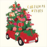 A festive illustration of a red car driven by a green Christmas tree laden with wrapped presents, with the words 'CHRISTMAS WISHES' in gold lettering on a cream background.