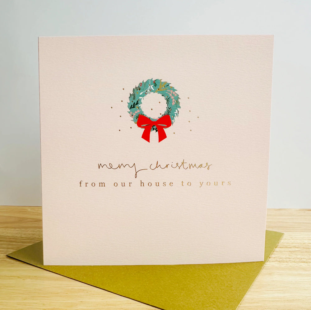 A cream card with a Christmas wreath and the words Merry Christmas from our house to yours.