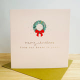 A cream card with a Christmas wreath and the words Merry Christmas from our house to yours.