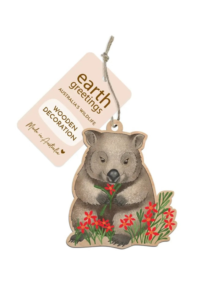 Wooden decoration of a wombat holding flowers with 'earth greetings' tag on a white background