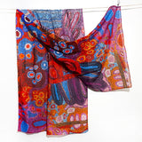 A lightweight sheer scarf with a vibrant, multicolored Aboriginal dot-art pattern, draped over a white line against a plain white background.