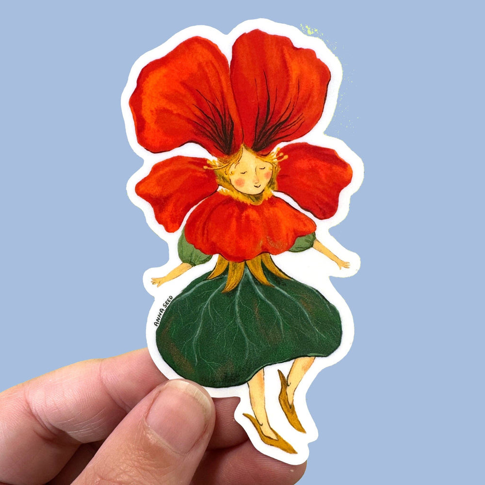 A die-cut sticker featuring a whimsical fairy-like figure with a large red flower head, gold hair, and a green leaf skirt, held by a hand against a light blue background.