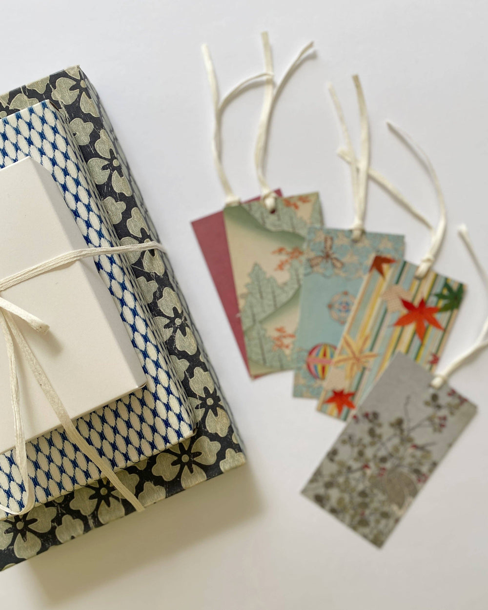 Japanese-style gift wrapping paper and matching gift tags with traditional patterns, tied with white string on a clean white background.