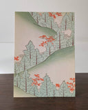 Woodblock print of a forest scene with trees and red flowers on a wooden surface.