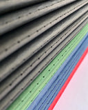 Close-up of layered fabric or textile strips in gray, green, blue, and red, stacked diagonally with visible stitched edges and small perforations.