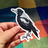 Hand holding a sticker of a black and white bird against a colorful fabric background