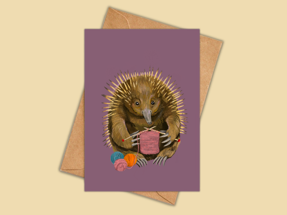 A rectangular card with a purple background featuring an illustration of an echidna holding knitting needles and yarn, shown with a brown envelope on a warm beige background.