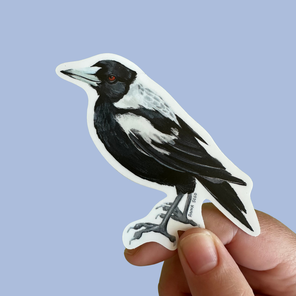 Hand holding a sticker of a black and white bird against a light blue background
