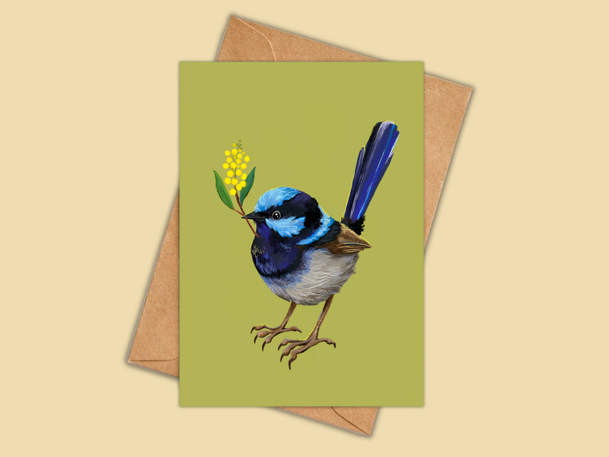 A greeting card featuring an illustration of a blue and white bird holding yellow flowers, shown with a brown kraft envelope on a warm beige background.