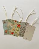 Four decorative paper gift tags with cream ribbons, displayed on a light gray background. Three tags feature colorful patterns of starfish, stripes, and botanical illustrations, while the rightmost tag is a simple beige card with 'to' and 'from' lines.