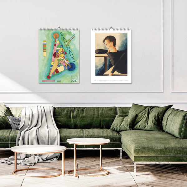 Two wall calendars displayed on a white wall above a green sofa in a living room.