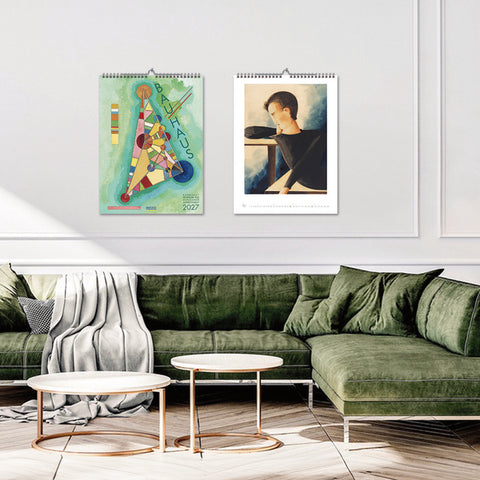Two wall calendars displayed on a white wall above a green sofa in a living room.