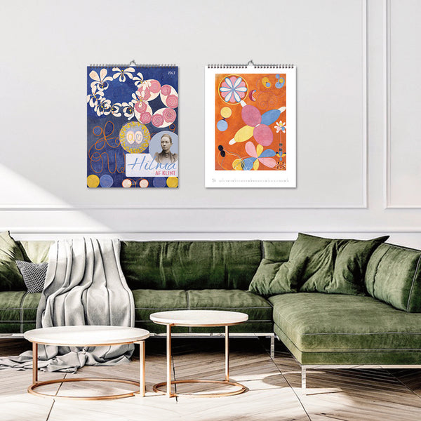 Two colorful wall calendars hanging on a white wall above a green sofa.