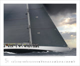 A close up of a large sailing boat with people sitting over the edge and dark clouds above.