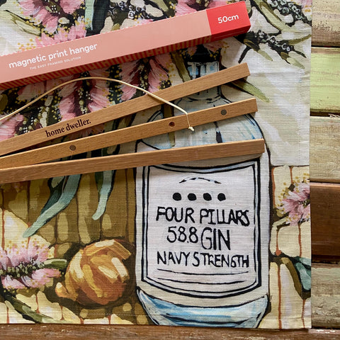 Bamboo hangers with 'Four Pillars 58.8 Gin Navy Strength' label on a floral background