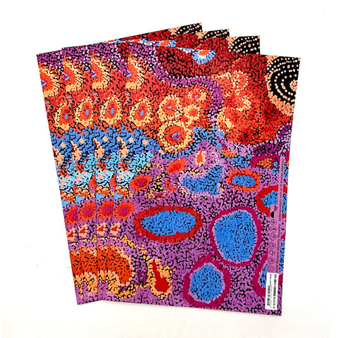 A stack of four folded sheets of wrapping paper featuring a vibrant Aboriginal dot art pattern with red, orange, blue, purple, and black dots on a white background.