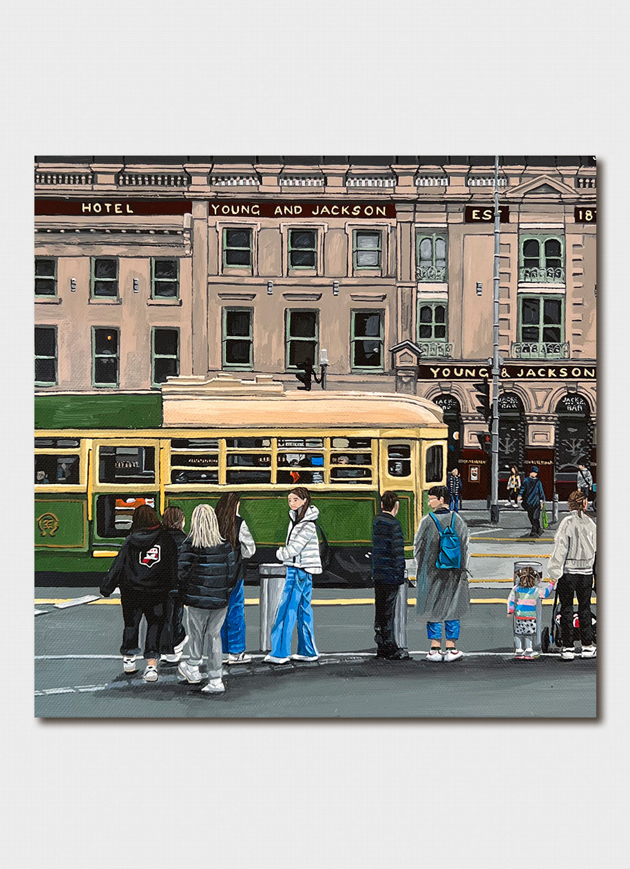 An old building with a green and yellow tram and people waiting on the street.