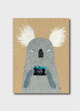 Luka Va notebook with a koala holding a camera on a natural kraft background.