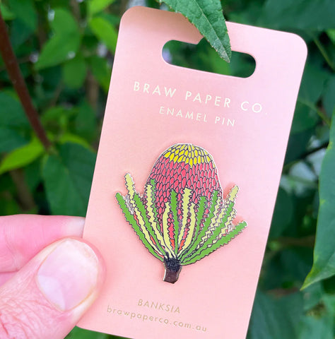 Enamel pin on a pink card with 'Braw Paper Co' branding, held against a green leafy background.