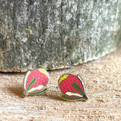 Strawberry-themed earrings on a wooden surface with a stone background