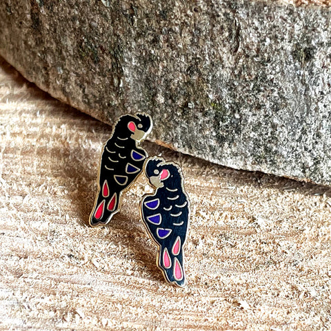 Two bird-shaped pins on a wooden surface with a stone background