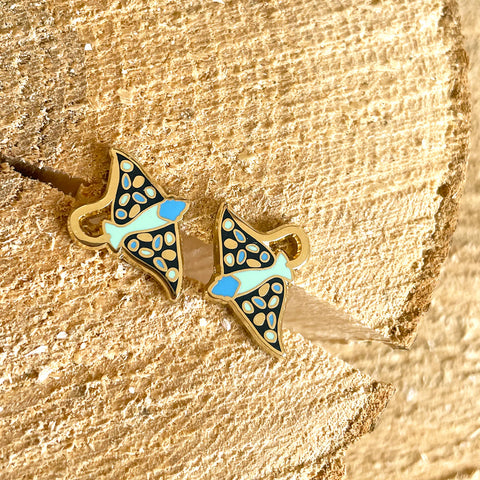 Butterfly-shaped earrings with gold, blue, and black design on a textured gold background