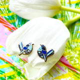 Blue bird-shaped pins on a colorful tie-dye background with white shells.