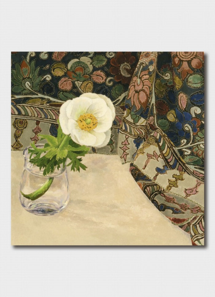 White flower in a glass on a textured surface with a patterned fabric background