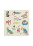 Different dog breeds in beds, wearing jackets and with toys, food and books on a card with words Happy Birthday in gold lettering