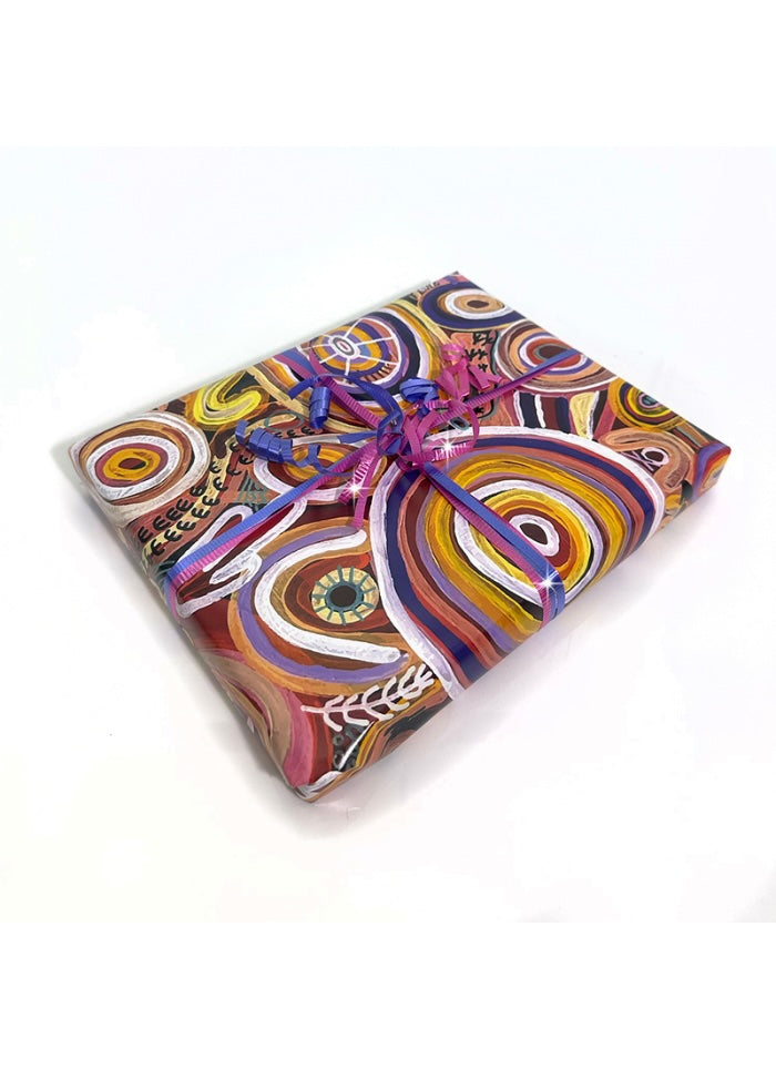 A gift box wrapped in vibrant, multicolored abstract patterned paper and tied with a purple ribbon, set against a plain white background.