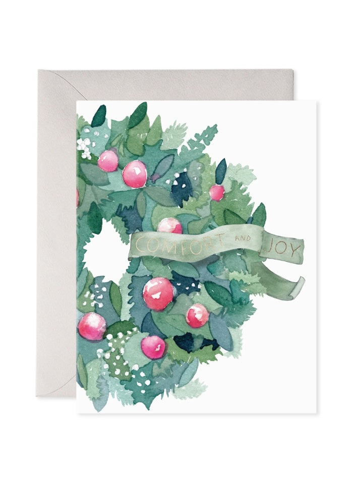 A wreath in greens and pink with a banner saying Comfort and Joy.