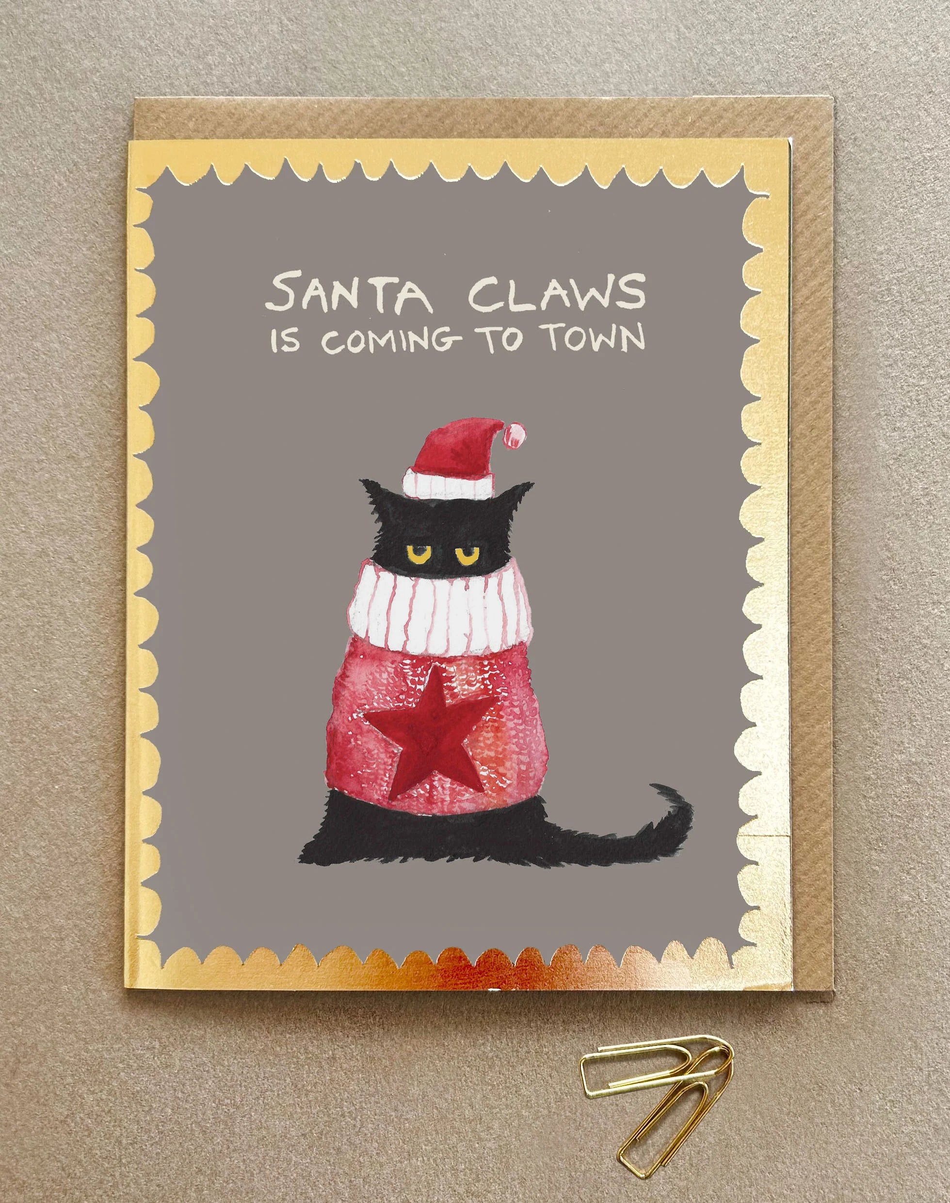 A Christmas card with a cat in a woollen jumper and santa hat and the words Santa Claws is coming to town