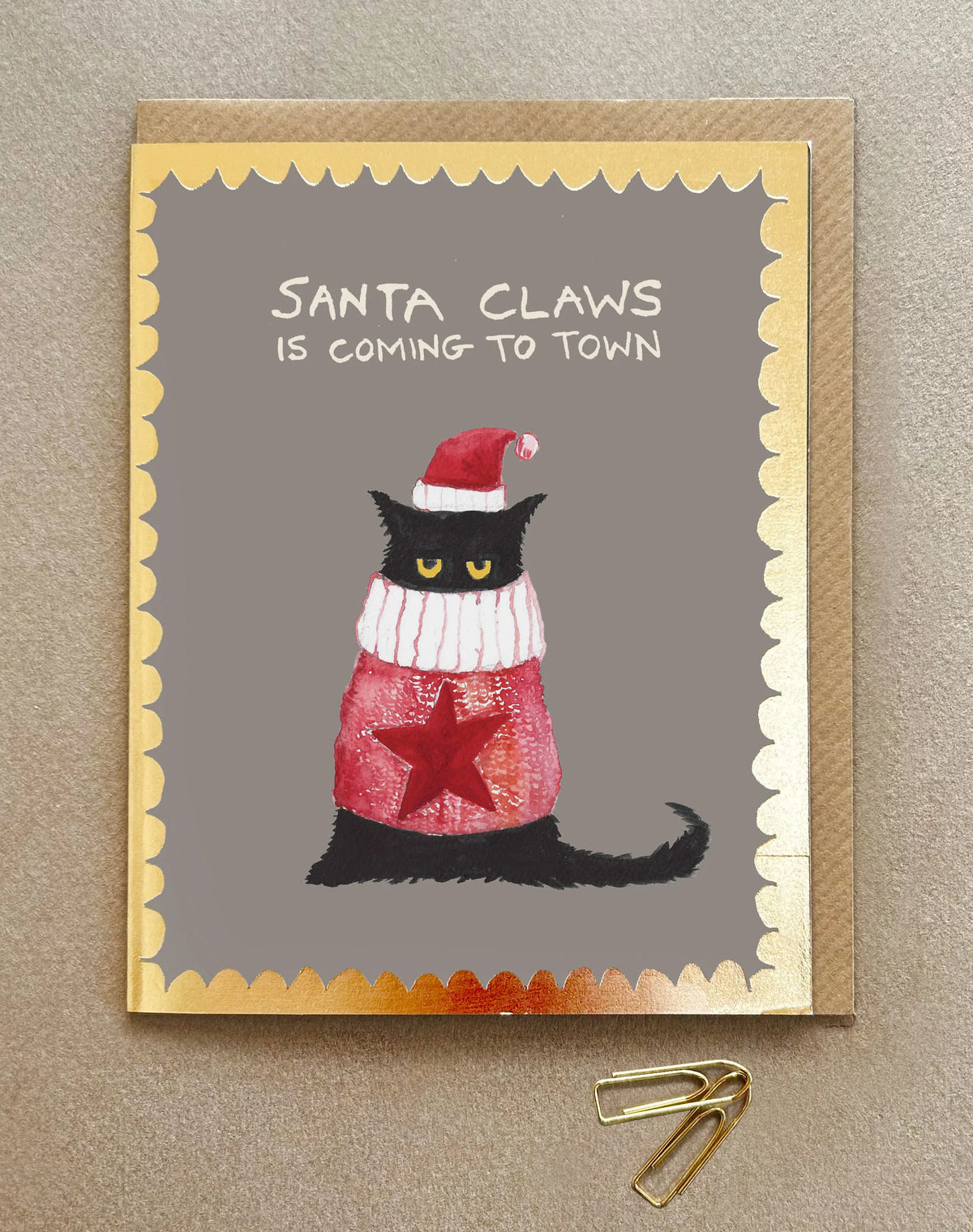 A Christmas card with a cat in a woollen jumper and santa hat and the words Santa Claws is coming to town