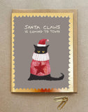 A Christmas card with a cat in a woollen jumper and santa hat and the words Santa Claws is coming to town