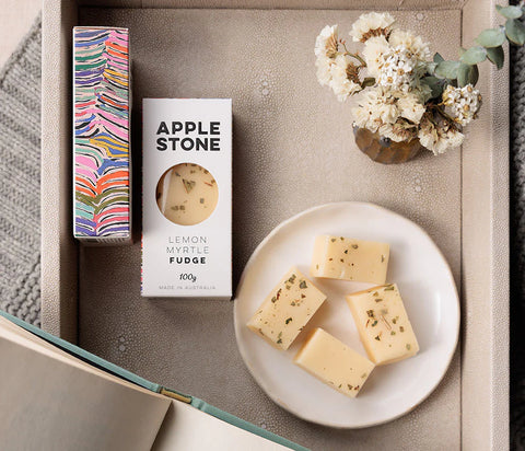 Box of Apple Stone lemon myrtle fudge on a textured surface with a plate of fudge and decorative elements.