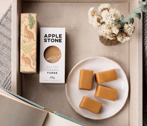 Apple Stone salted caramel fudge with packaging on a textured surface with flowers.