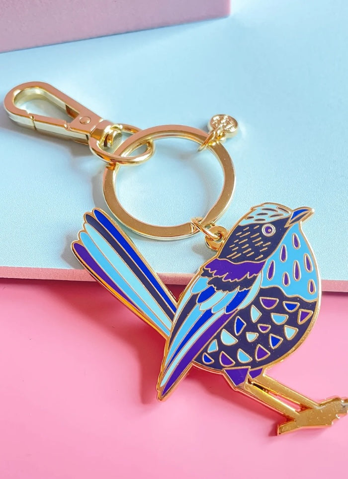 Bird-shaped keychain with gold accents on a pink and blue background