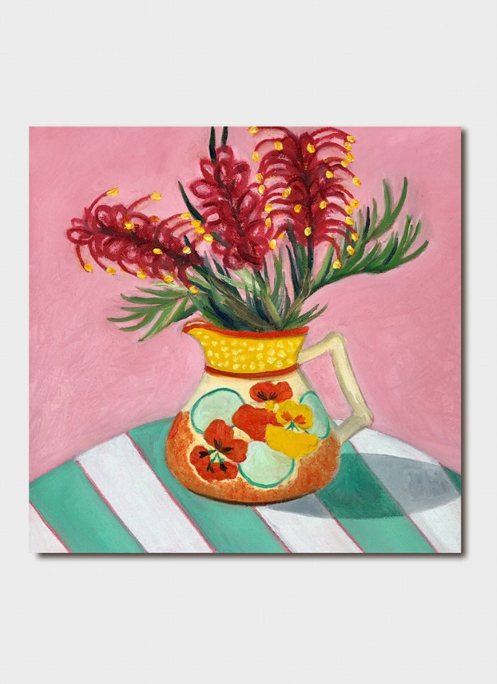 Orange vase with flowers on it and grevillea in it on a table with a green and white striped tablecloth.